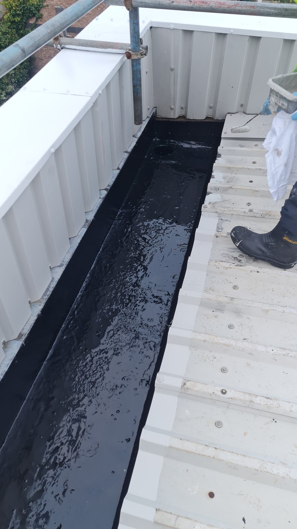 Liquid gutter lining being applied along an industrial valley gutter
